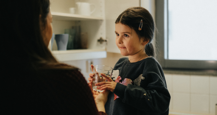 Barn får ett glas vatten av sin mamma.